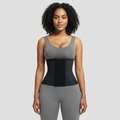 Woman wearing a black waist trainer over a gray tank top and leggings on a light gray background